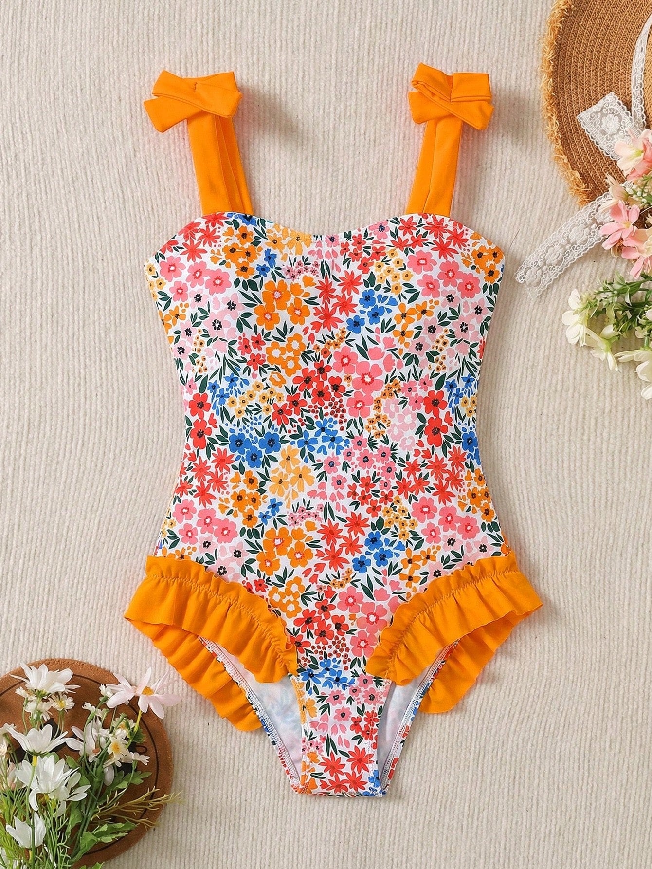 Girls' multicolor one-piece swimsuit with floral plant print, bow detail, asymmetrical ruffle accent, strap neckline, and lined body for beach vacations.