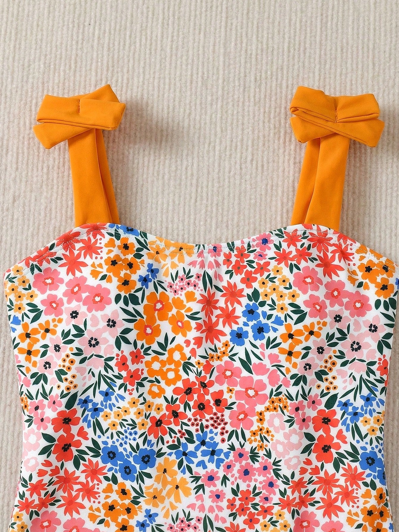 Girls' multicolor one-piece swimsuit with floral plant print, bow detail, asymmetrical ruffle accent, strap neckline, and lined body for beach vacations.