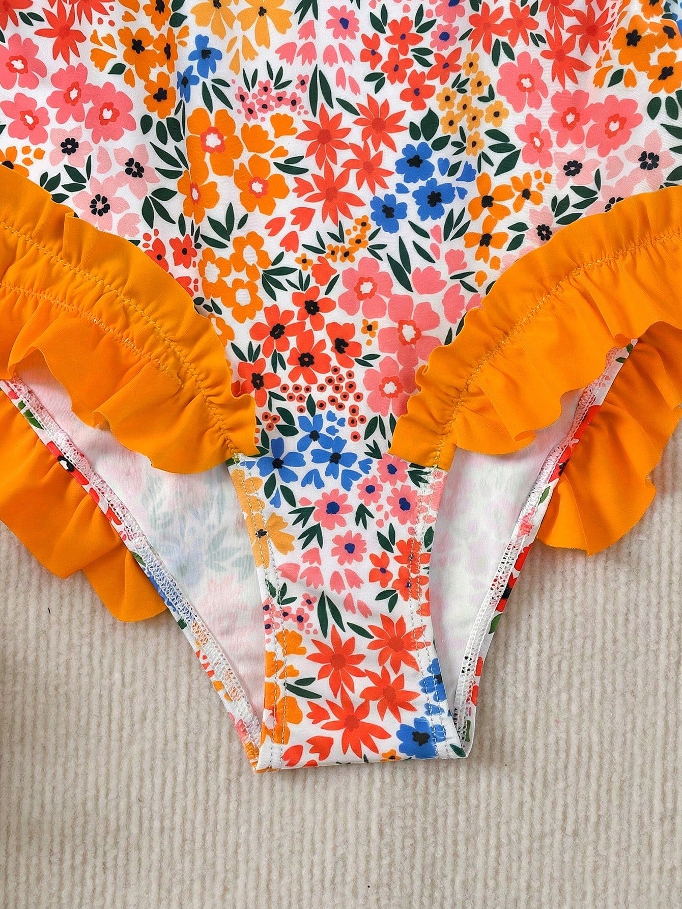 Girls' multicolor one-piece swimsuit with floral plant print, bow detail, asymmetrical ruffle accent, strap neckline, and lined body for beach vacations.