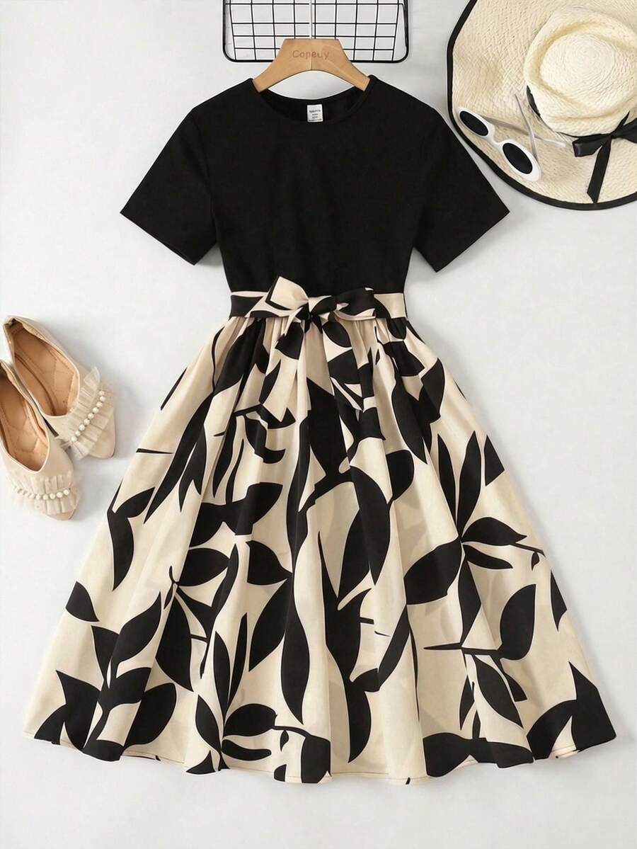 Tween girl wearing an apricot short sleeve A-line dress featuring a round neck, high waist with a belt, and flared hem.