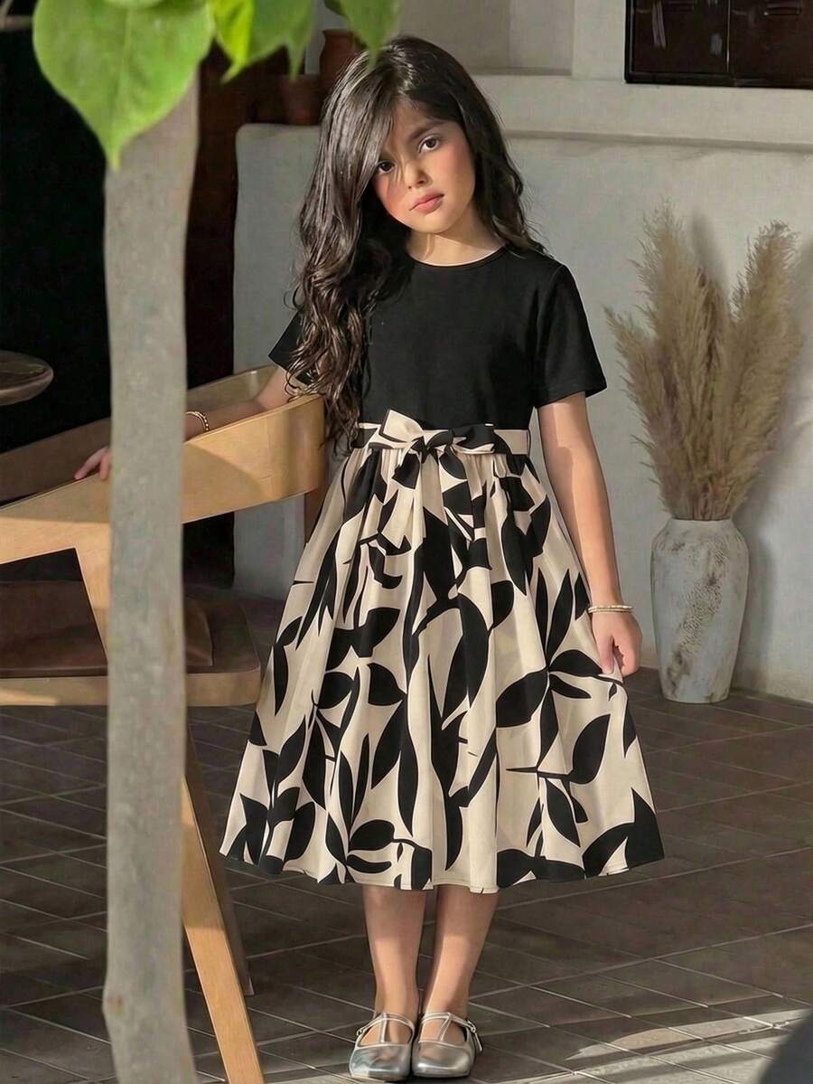 Tween girl wearing an apricot short sleeve A-line dress featuring a round neck, high waist with a belt, and flared hem.
