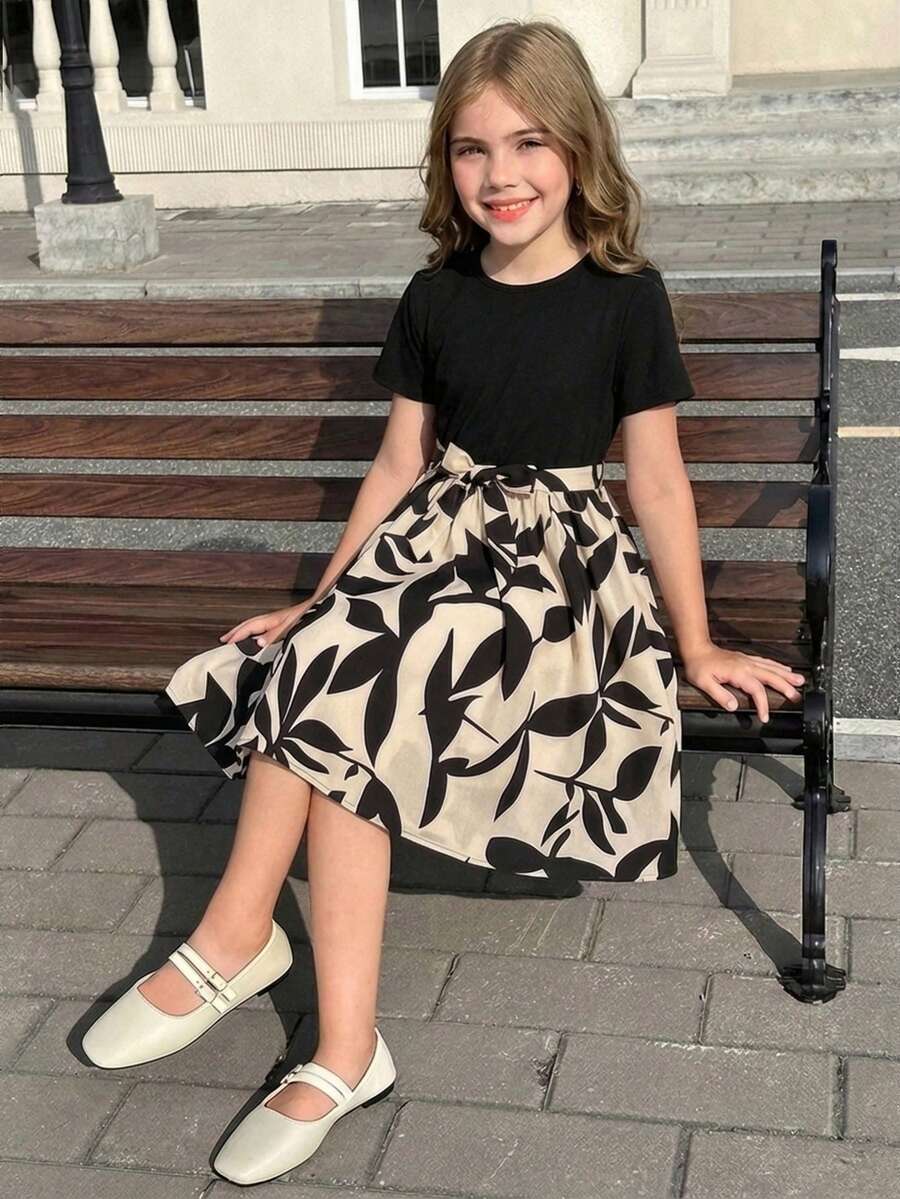 Tween girl wearing an apricot short sleeve A-line dress featuring a round neck, high waist with a belt, and flared hem.