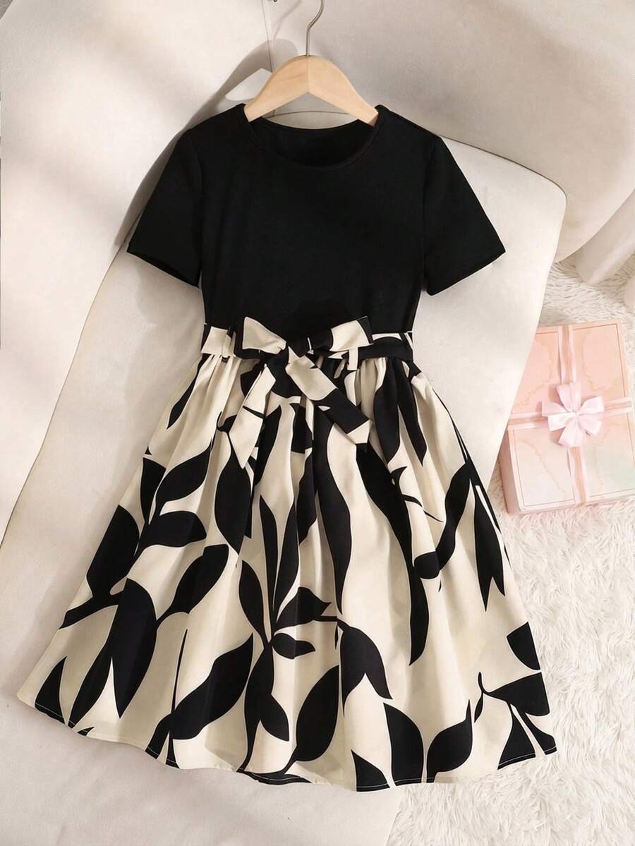 Tween girl wearing an apricot short sleeve A-line dress featuring a round neck, high waist with a belt, and flared hem.