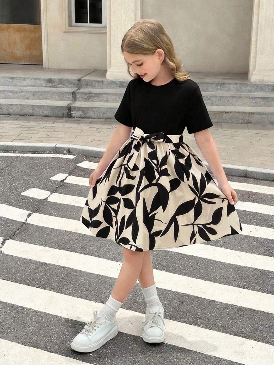 Tween girl wearing an apricot short sleeve A-line dress featuring a round neck, high waist with a belt, and flared hem.