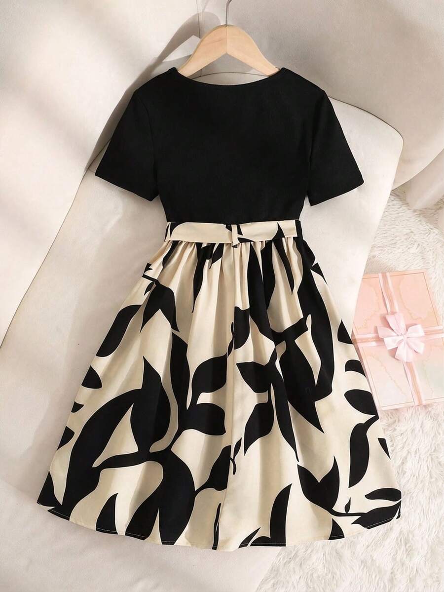 Tween girl wearing an apricot short sleeve A-line dress featuring a round neck, high waist with a belt, and flared hem.
