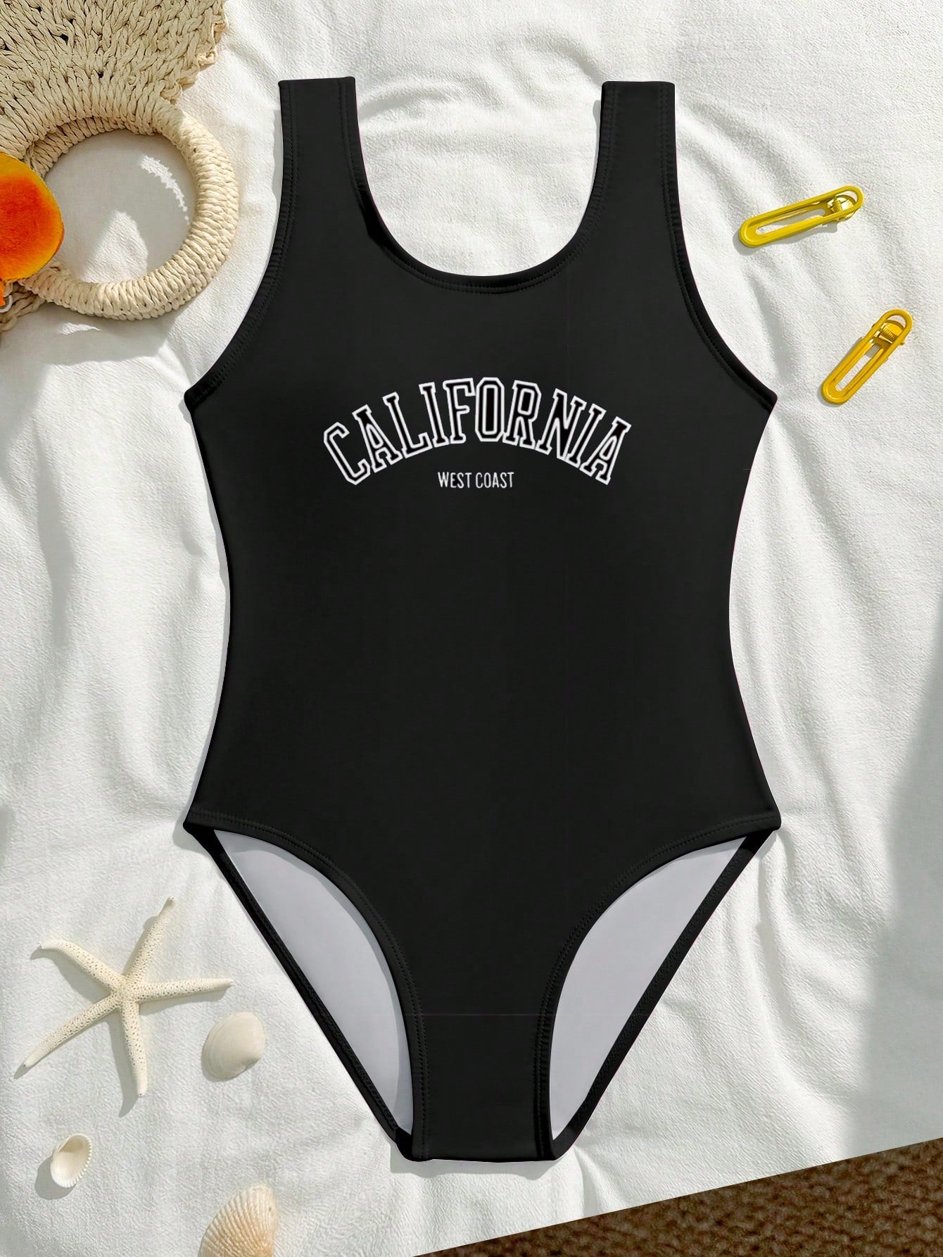 Tween girls one-piece swimsuit with a black base and multicolor tropical plant print featuring bamboo, palm leaves, plumeria flowers, scoop neck, and wide straps.