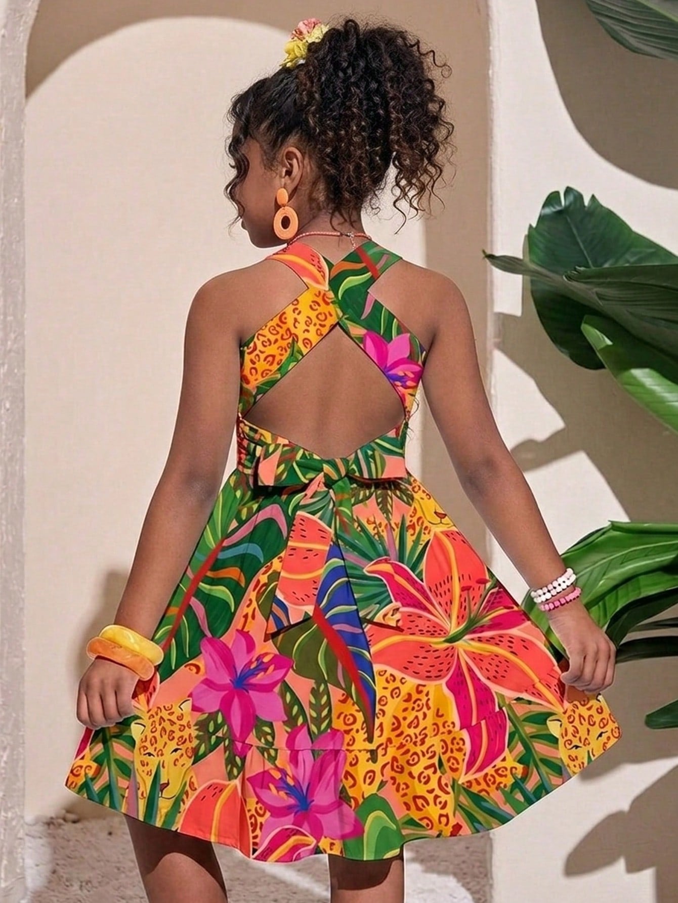 Pink sleeveless tween girls vacation dress with all-over fruit and vegetable print, strap neckline, belted high waist, cut-out detail, and flared ruffle hem.