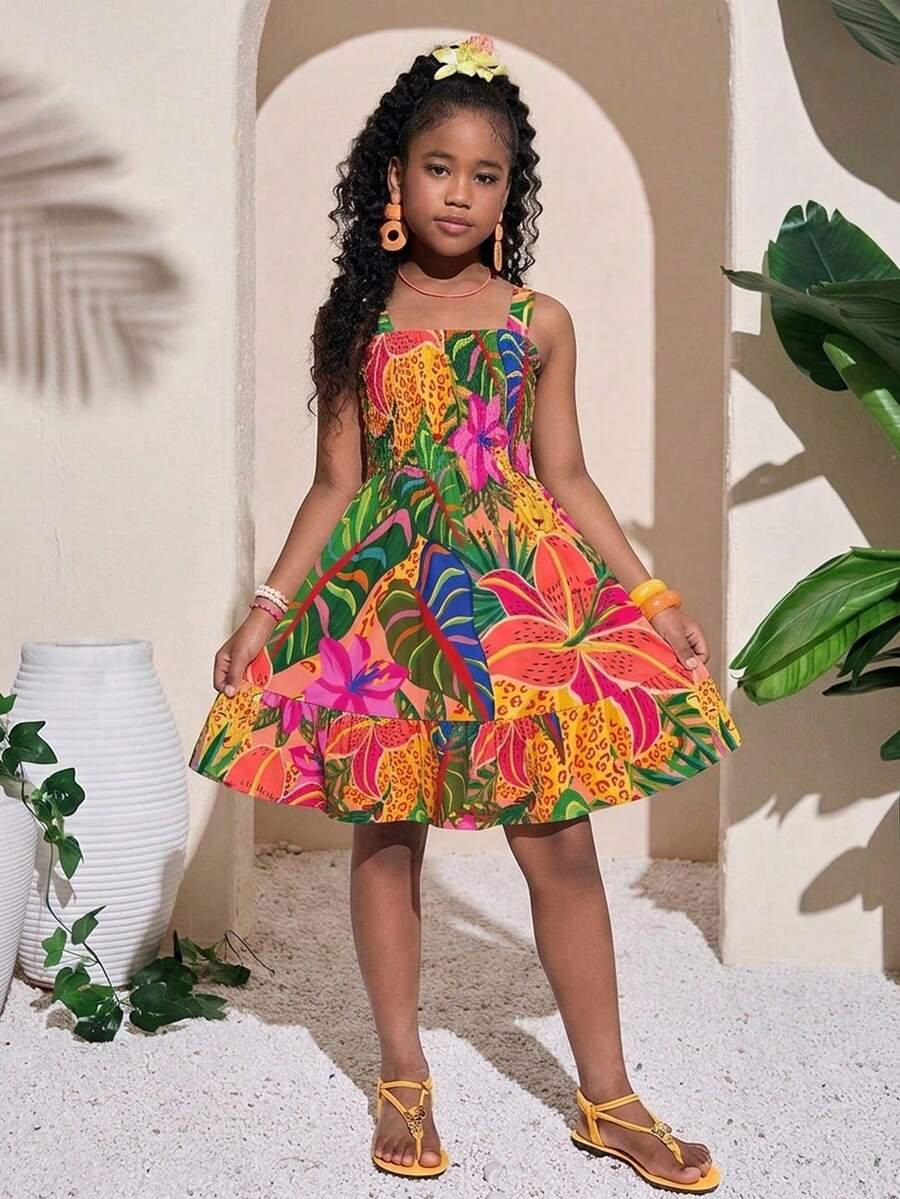 Pink sleeveless tween girls vacation dress with all-over fruit and vegetable print, strap neckline, belted high waist, cut-out detail, and flared ruffle hem.