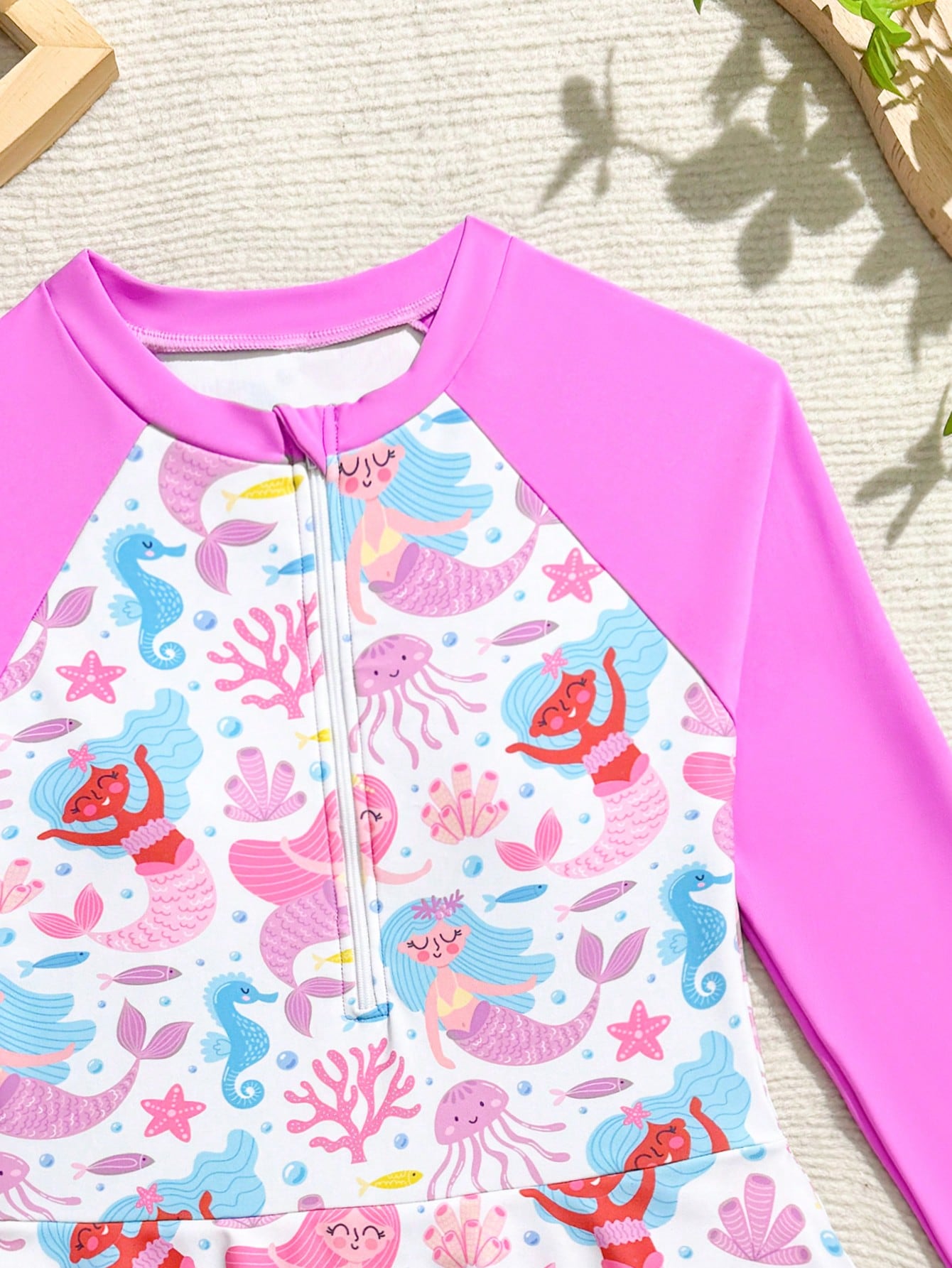 Tween girls one-piece rash guard swimsuit with long sleeves, high neck, front zipper, and ocean shell graphic print in a fitted style for beach, swimming, and vacation wear.