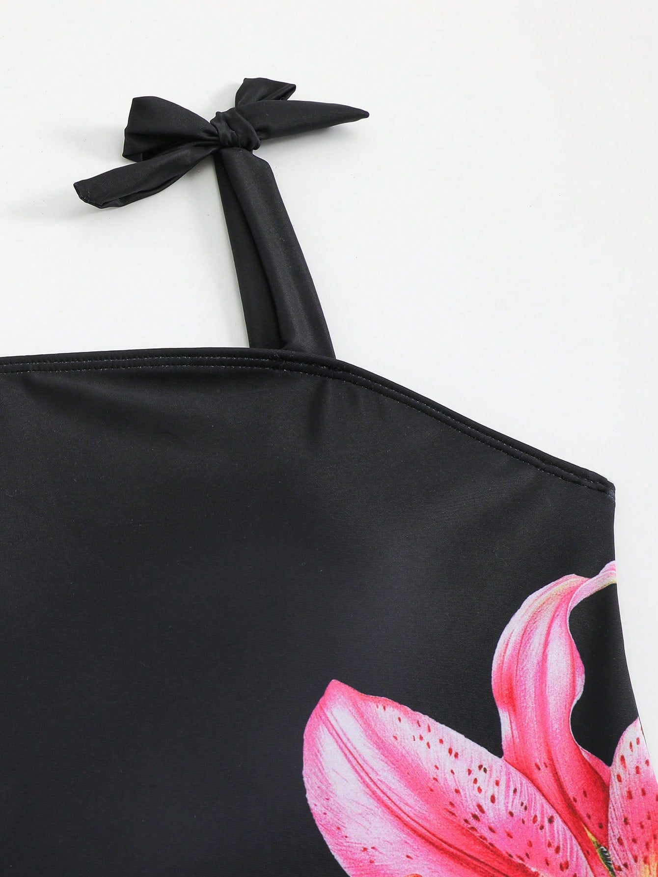 Tween girl black floral one-piece swimsuit set with spaghetti straps, asymmetrical detail, bow decor, and mid-waist bottom for beach, pool, and summer vacation wear.