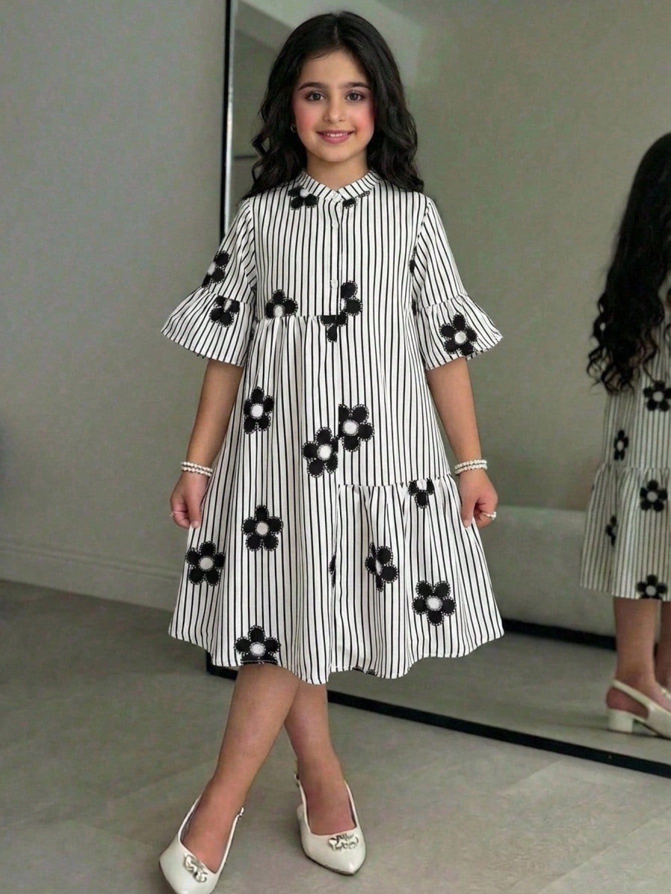 Tween girl wearing a black striped smock shirt dress with flounce half sleeves, a stand collar, and a ruffled hem.