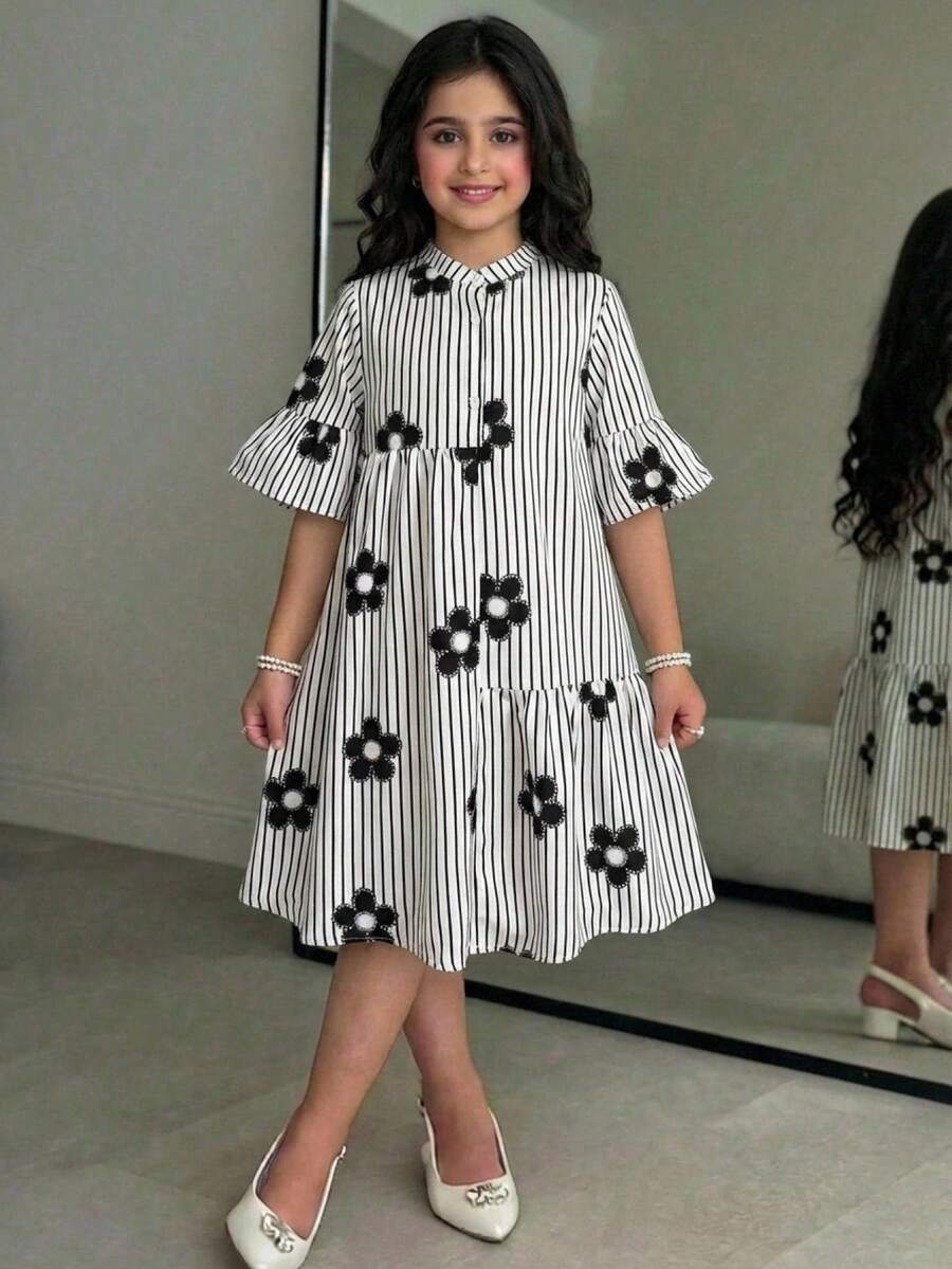 Tween girl wearing a black striped smock shirt dress with flounce half sleeves, a stand collar, and a ruffled hem.