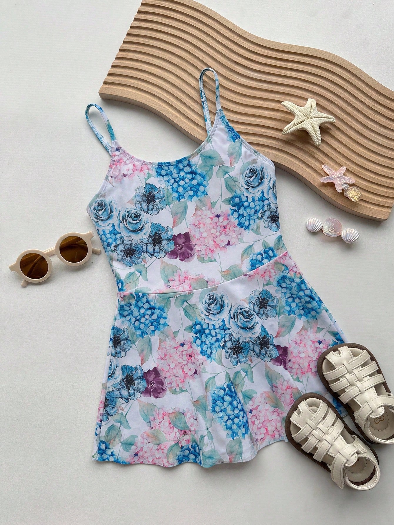 Baby blue graphic one-piece swimsuit for tween girls with spaghetti straps, asymmetrical detail, fitted shape, and vacation beachwear style