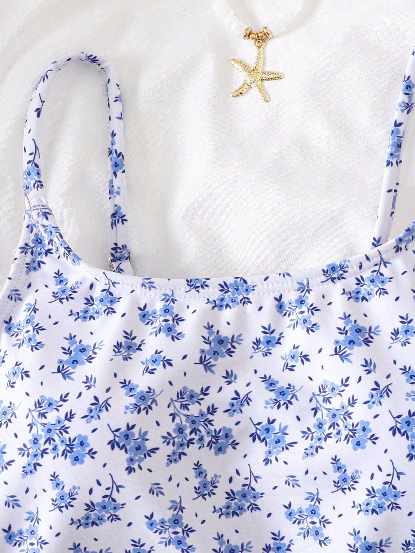 Baby blue floral ruffle one-piece swimsuit for tween girls with bow decor, spaghetti straps, all-over print, and fitted vacation beachwear style.