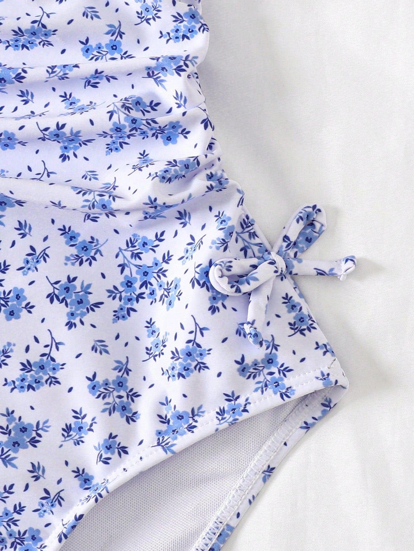 Baby blue floral ruffle one-piece swimsuit for tween girls with bow decor, spaghetti straps, all-over print, and fitted vacation beachwear style.