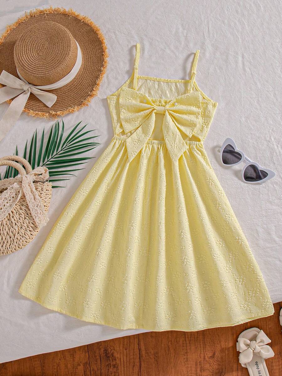 Tween girl wearing an apricot floral print sleeveless mini cami dress featuring spaghetti straps, a shirred high waist, flounce hem, and a bow back detail.