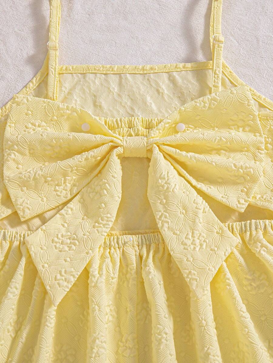 Tween girl wearing an apricot floral print sleeveless mini cami dress featuring spaghetti straps, a shirred high waist, flounce hem, and a bow back detail.