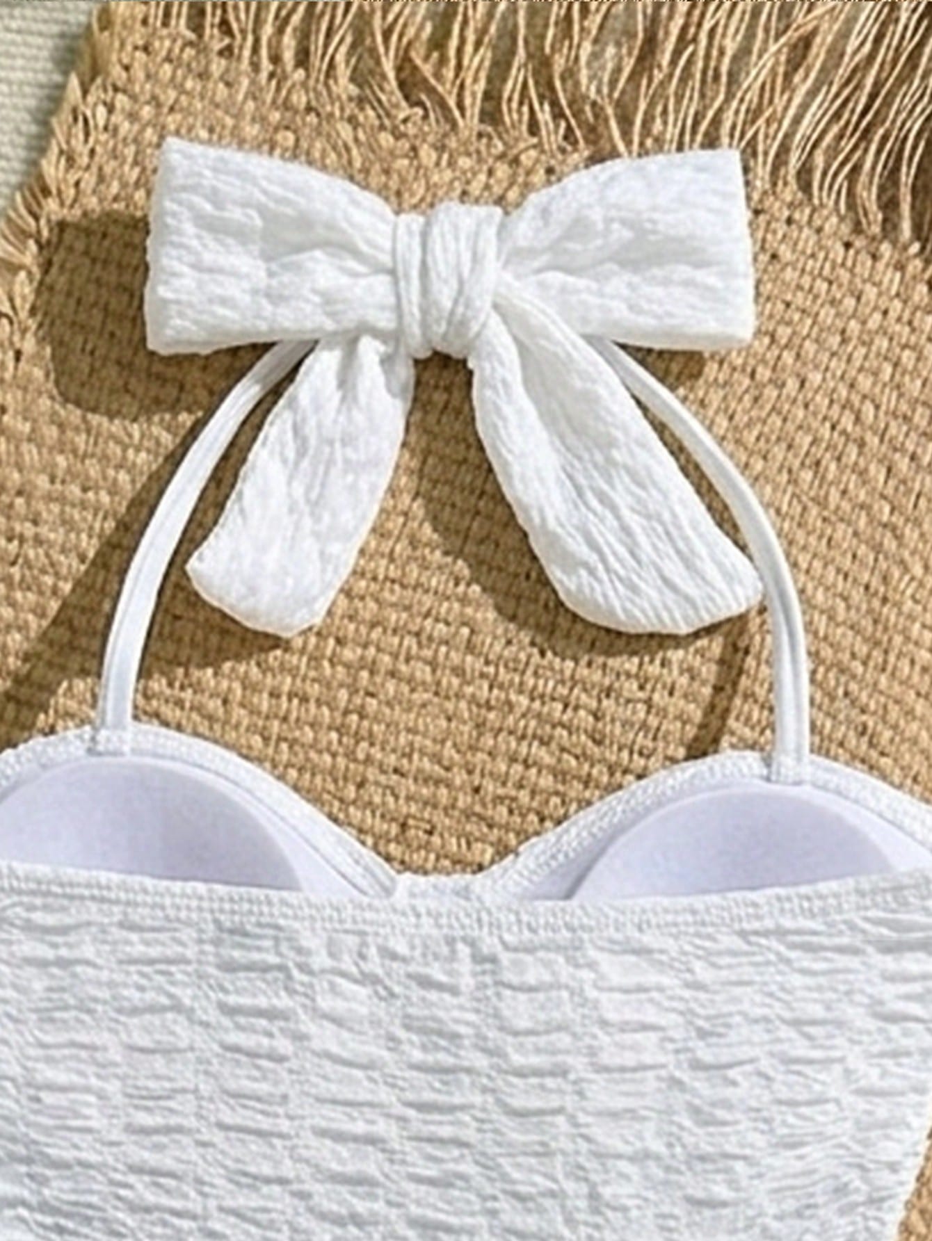 White tween girls one-piece swimsuit with textured fabric, spaghetti straps, tie bow detail, halter style, and open back for summer beachwear.