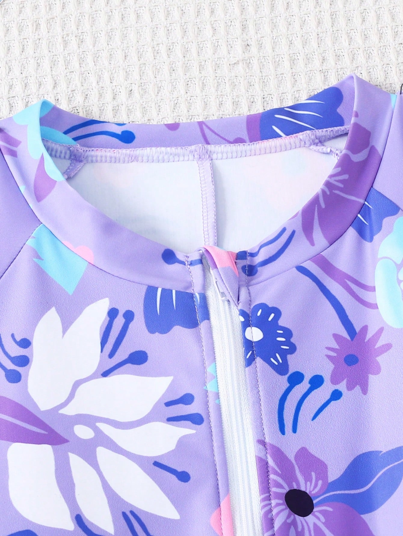 Black and white one-piece rashguard swimsuit for tween girls with short sleeves, high neck, zipper detail, fitted shape, and shorts-style bottom.