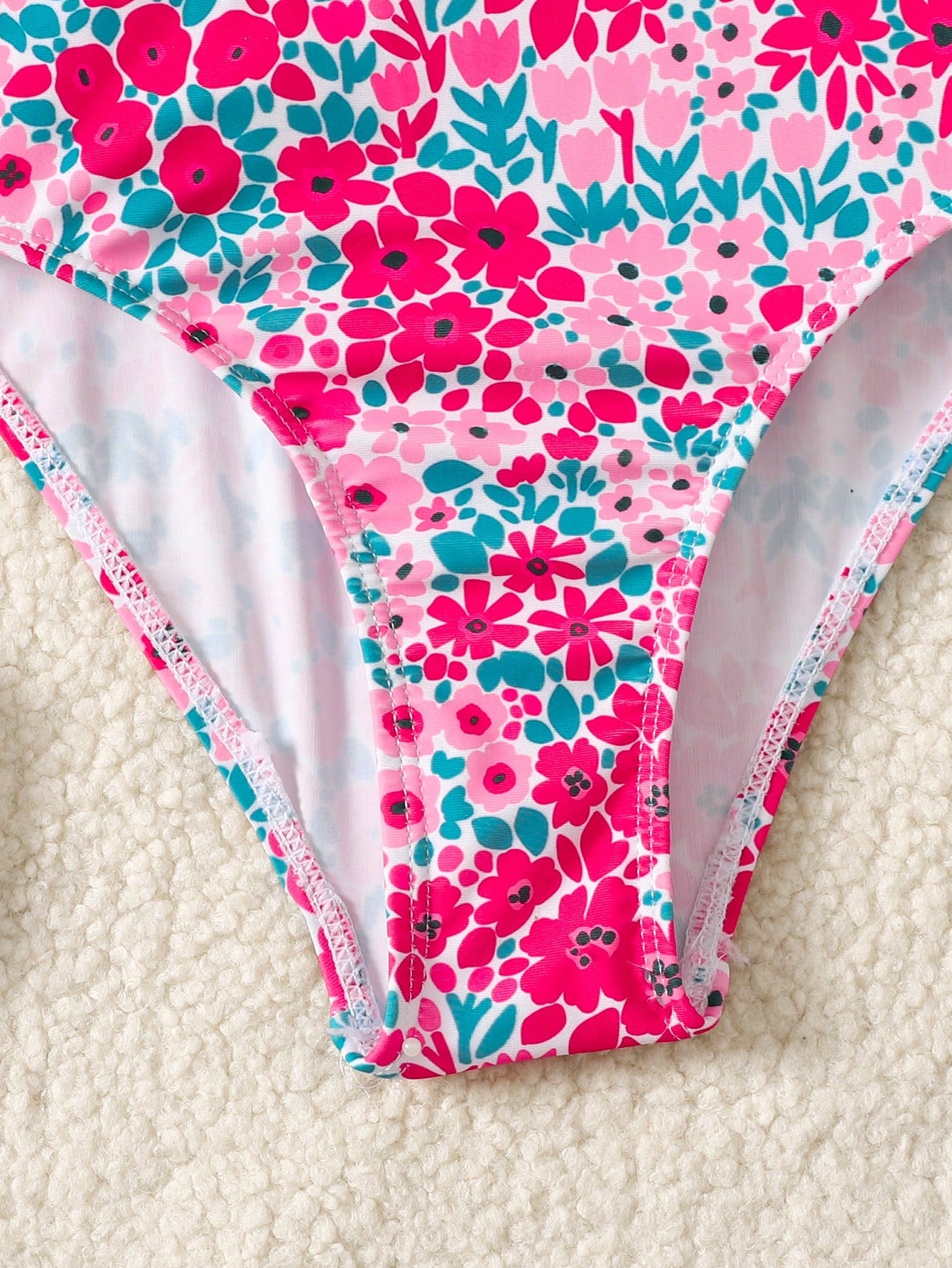 Tween girl floral print one-piece swimsuit with twist front, spaghetti straps, fitted shape, and multicolor all-over hibiscus-inspired pattern for beach and pool wear.