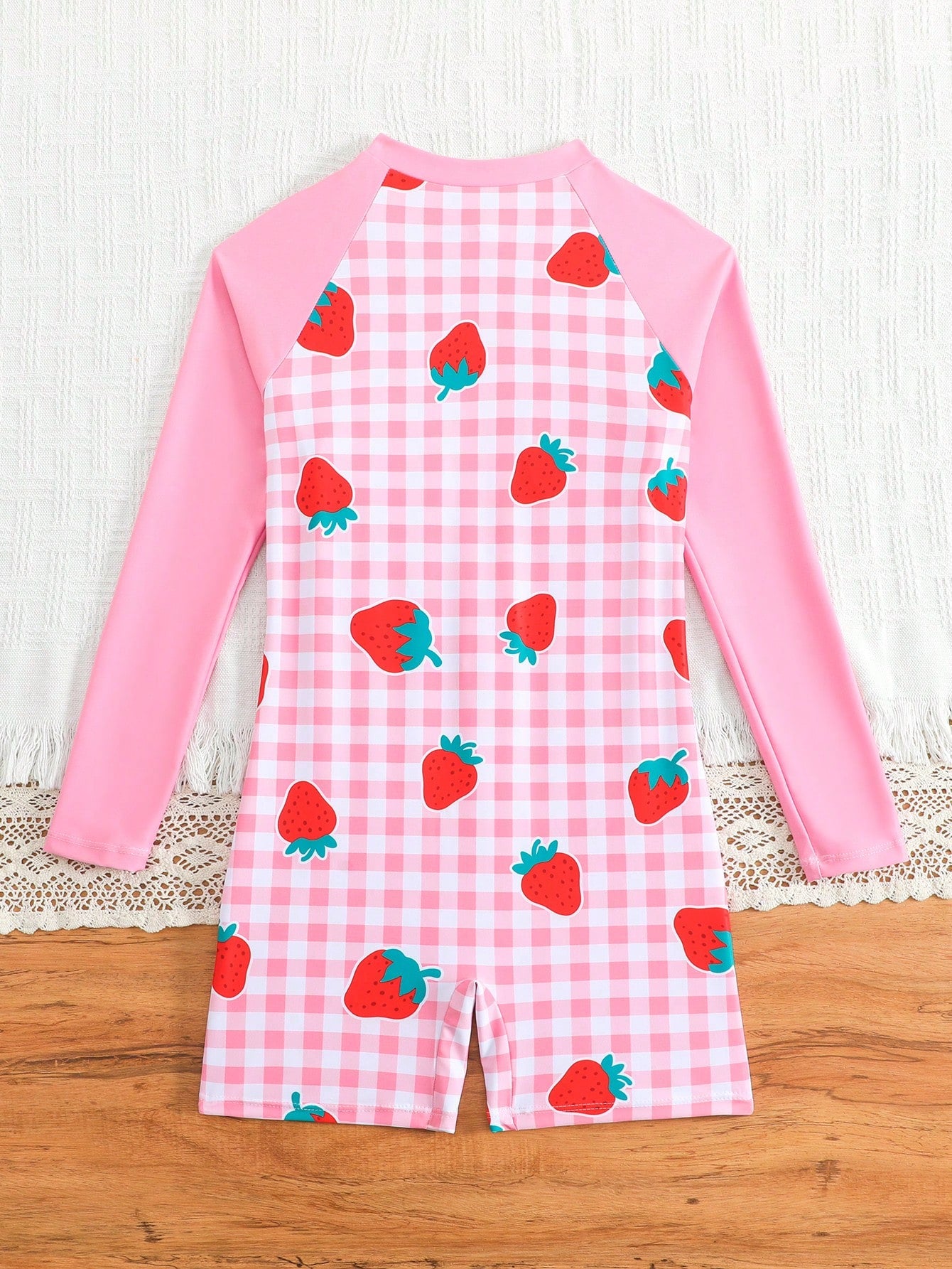 Tween girls one-piece swimsuit featuring a high neck, long sleeves, and shorts bottom, with a back zipper and strawberry plaid digital print on stretch knit fabric. Designed for swimming, vacation, and summer wear.