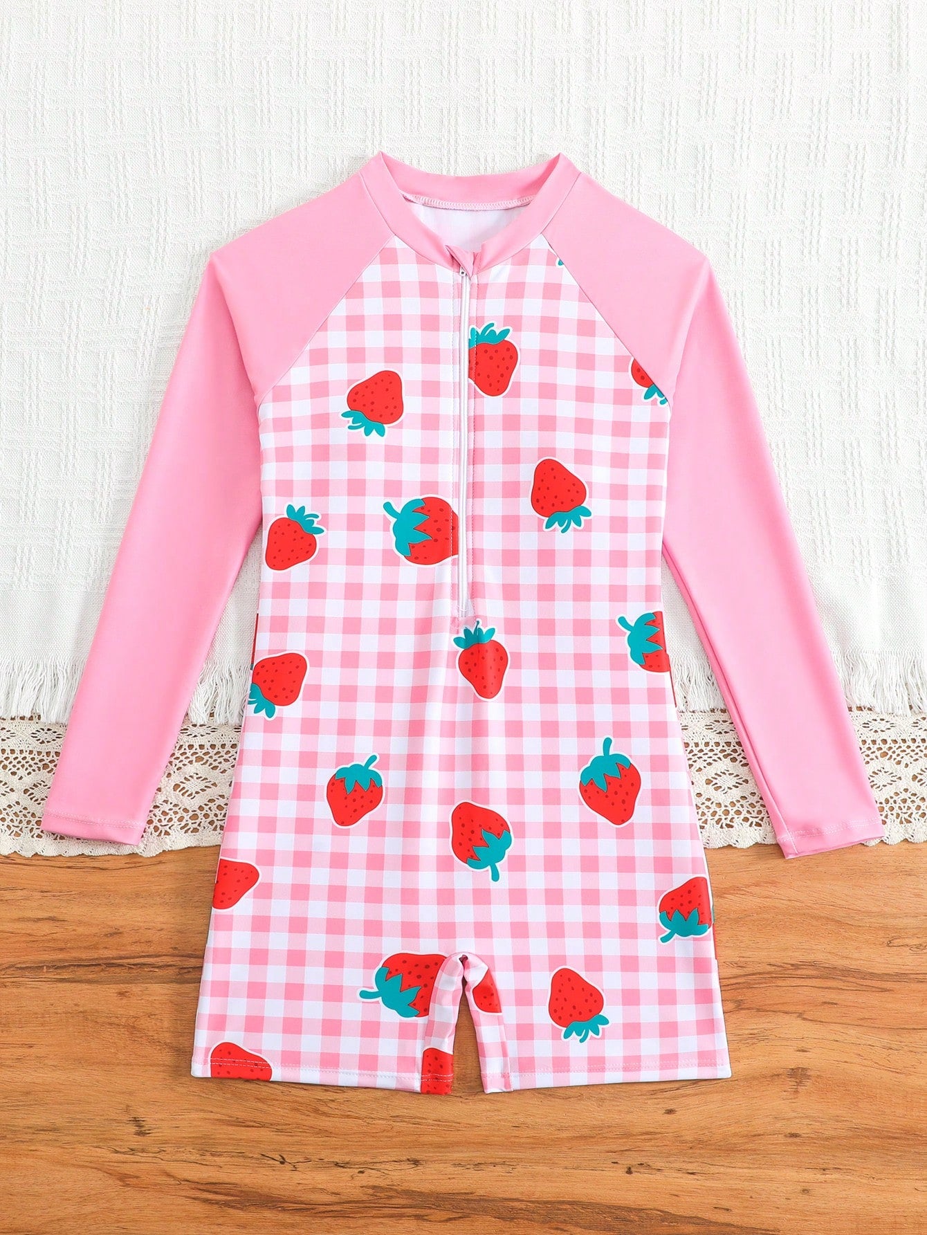 Tween girls one-piece swimsuit featuring a high neck, long sleeves, and shorts bottom, with a back zipper and strawberry plaid digital print on stretch knit fabric. Designed for swimming, vacation, and summer wear.