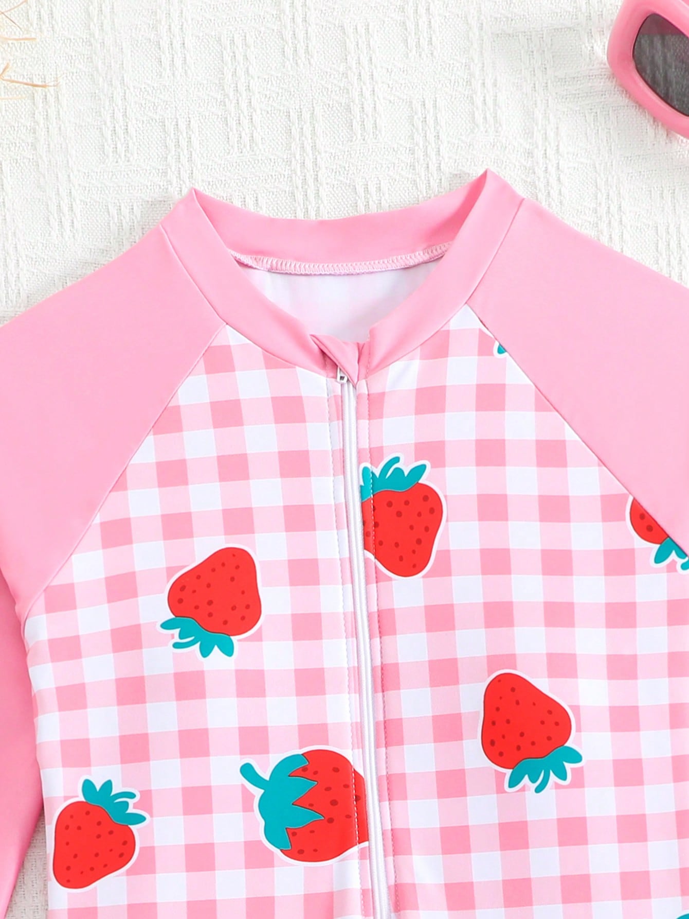Tween girls one-piece swimsuit featuring a high neck, long sleeves, and shorts bottom, with a back zipper and strawberry plaid digital print on stretch knit fabric. Designed for swimming, vacation, and summer wear.