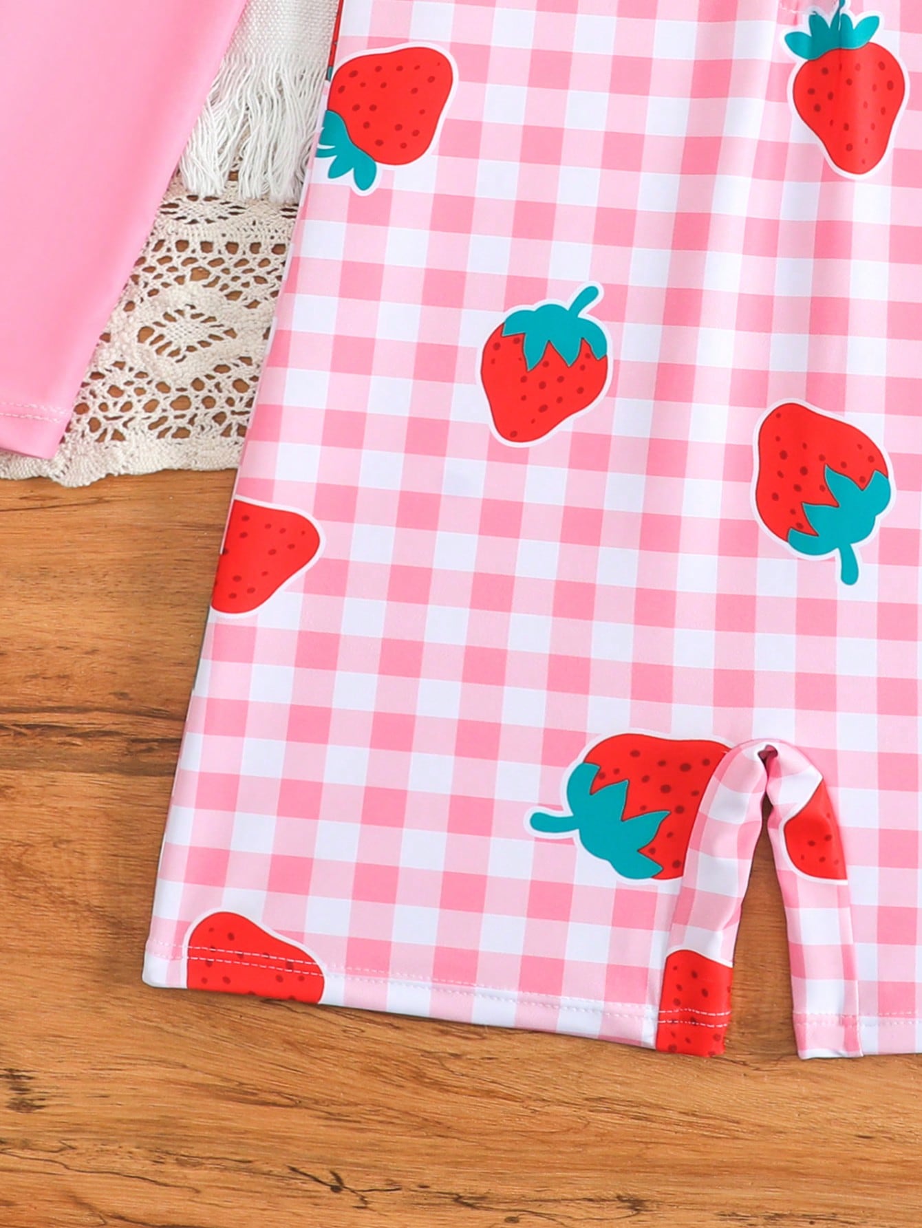 Tween girls one-piece swimsuit featuring a high neck, long sleeves, and shorts bottom, with a back zipper and strawberry plaid digital print on stretch knit fabric. Designed for swimming, vacation, and summer wear.