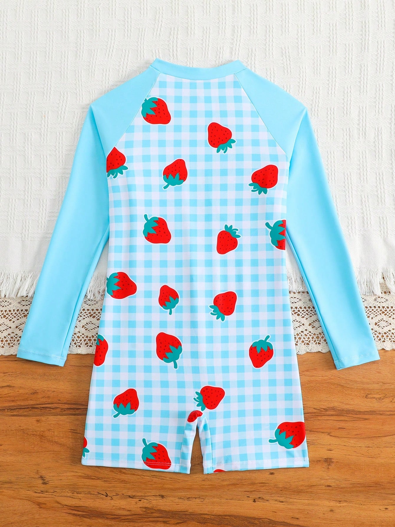 Tween girls one-piece swimsuit featuring a high neck, long sleeves, and shorts bottom, with a back zipper and strawberry plaid digital print on stretch knit fabric. Designed for swimming, vacation, and summer wear.