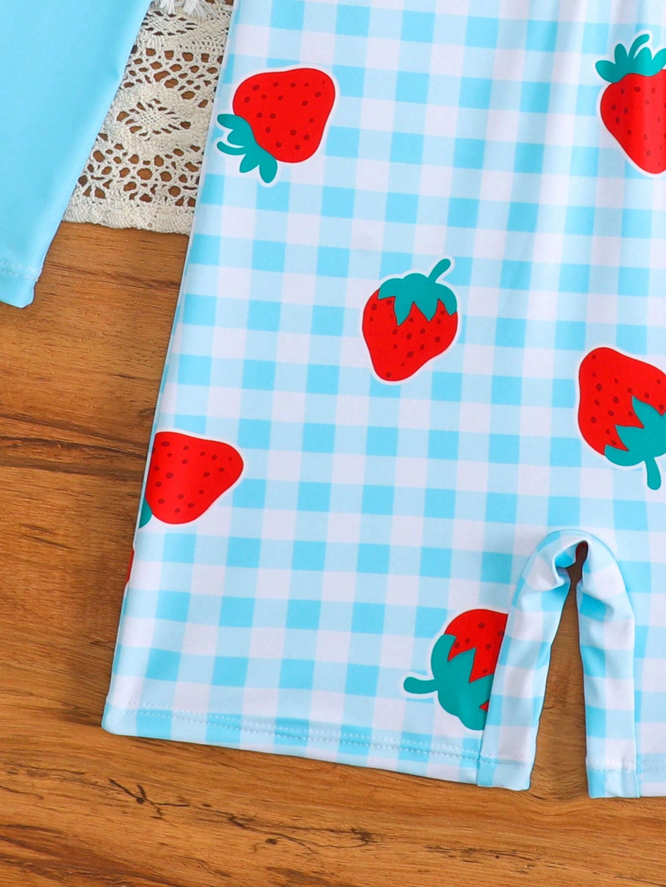 Tween girls one-piece swimsuit featuring a high neck, long sleeves, and shorts bottom, with a back zipper and strawberry plaid digital print on stretch knit fabric. Designed for swimming, vacation, and summer wear.