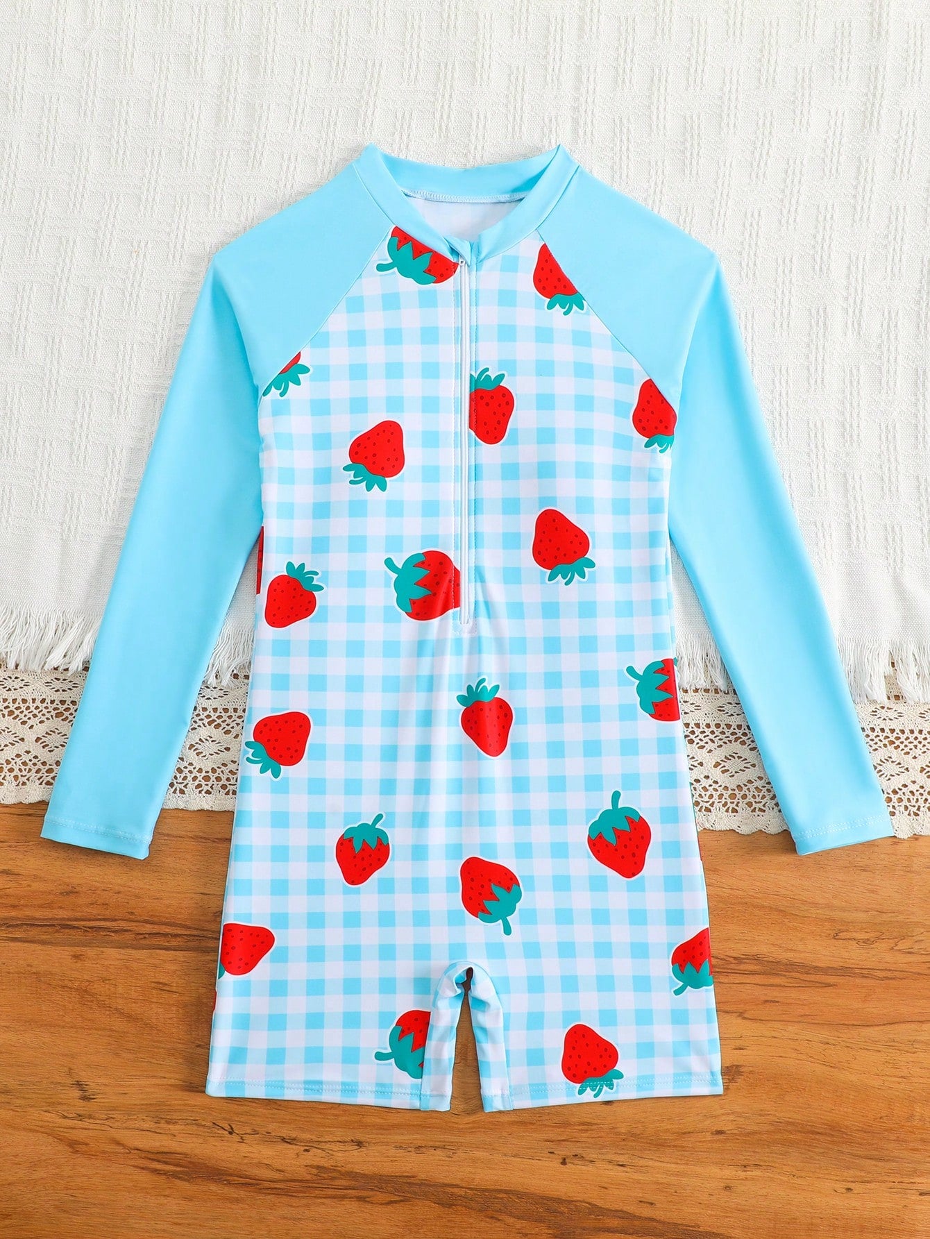 Tween girls one-piece swimsuit featuring a high neck, long sleeves, and shorts bottom, with a back zipper and strawberry plaid digital print on stretch knit fabric. Designed for swimming, vacation, and summer wear.