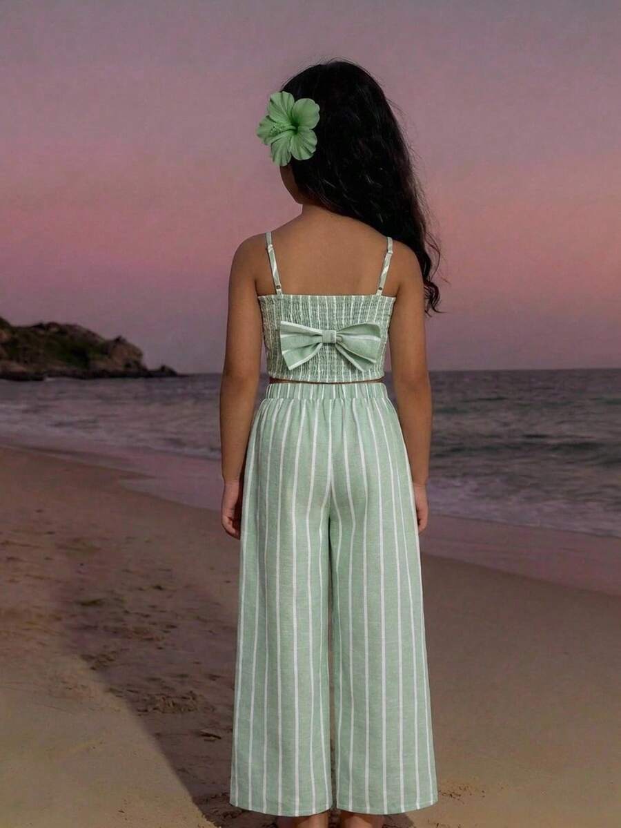 Tween girl wearing a black sleeveless spaghetti strap camisole top with 3D bow decor and matching leopard print wide leg long pants.