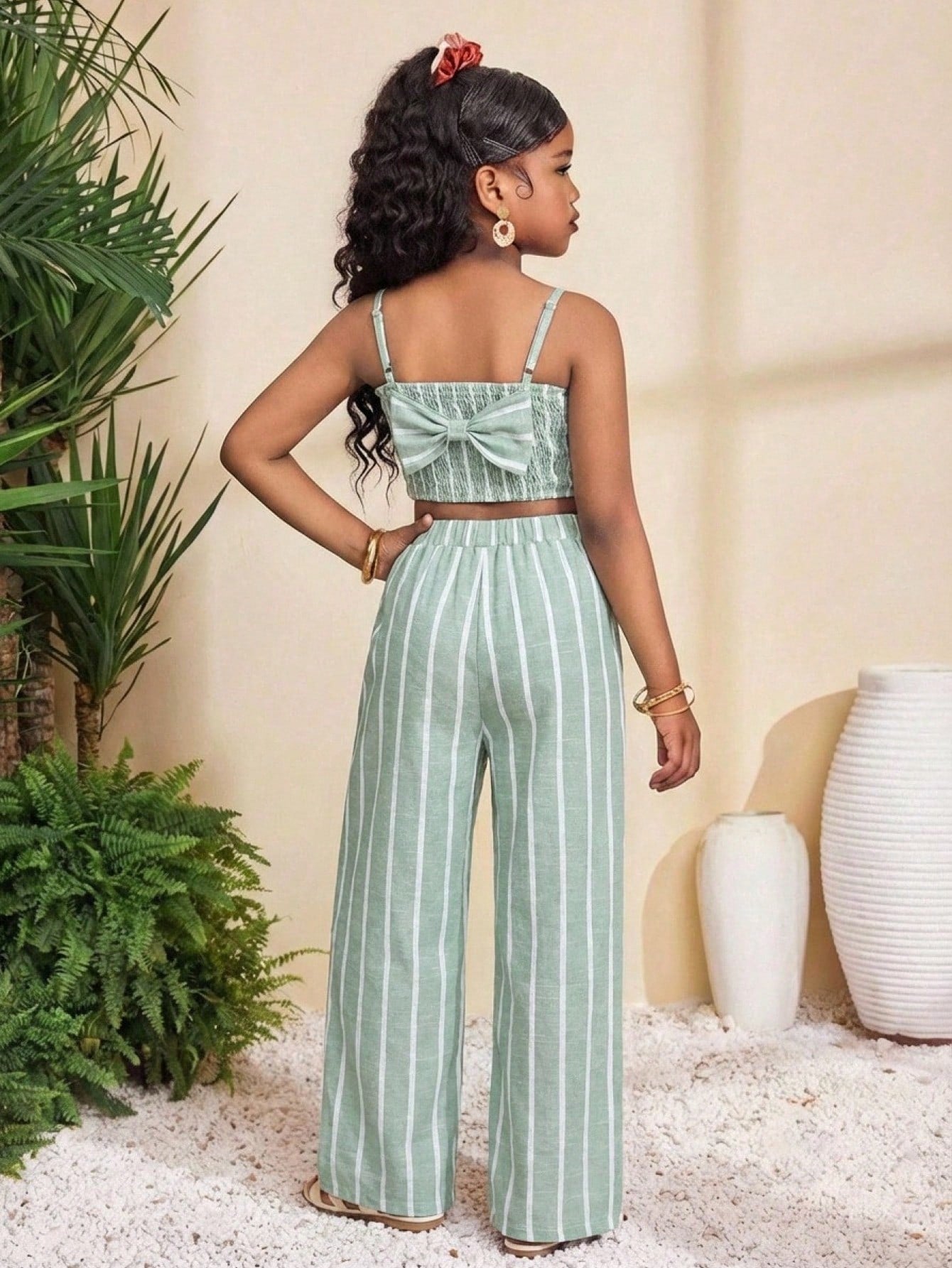 Tween girl wearing a black sleeveless spaghetti strap camisole top with 3D bow decor and matching leopard print wide leg long pants.
