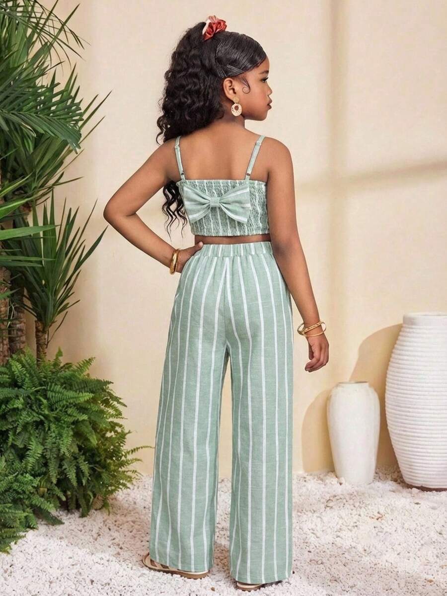 Tween girl wearing a black sleeveless spaghetti strap camisole top with 3D bow decor and matching leopard print wide leg long pants.