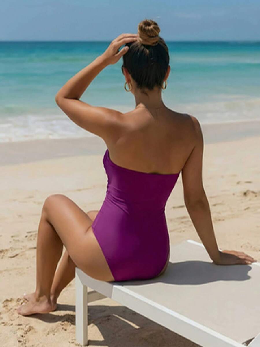 Woman wearing an elegant green solid color backless one-piece swimsuit with bandeau neckline and high waist design.