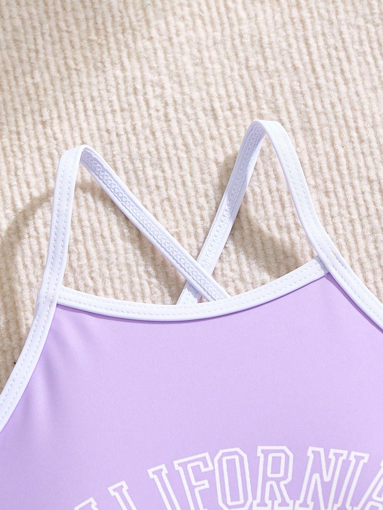 Girls' mauve purple one-piece swimsuit with swim shorts, spaghetti straps, contrast piping, letter pattern, and sleeveless vacation swimwear design.