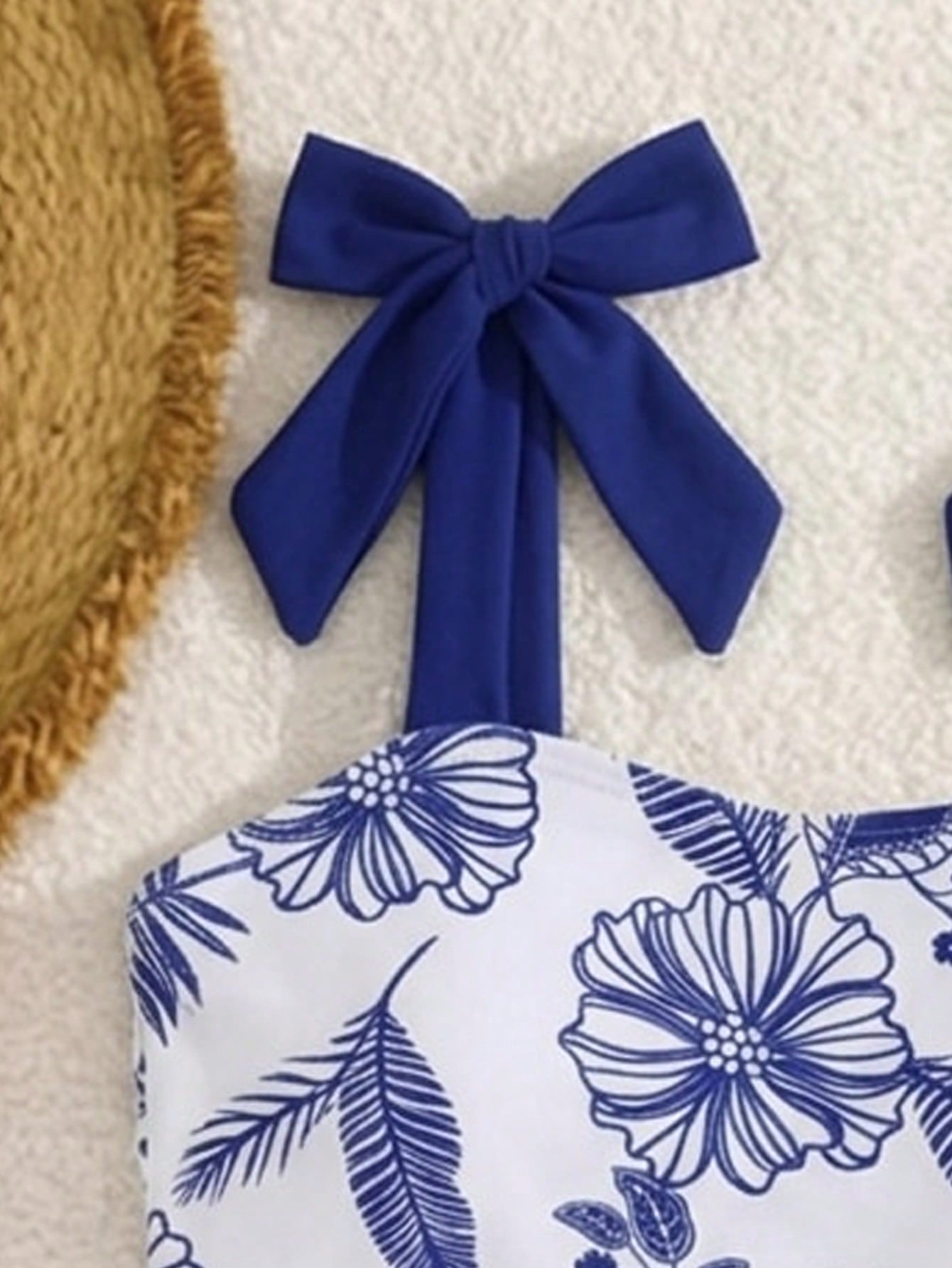 Navy blue tween girls one-piece swimsuit with all-over floral print, bow decor, strap neckline, and shorts-style bottom for summer vacation beachwear.