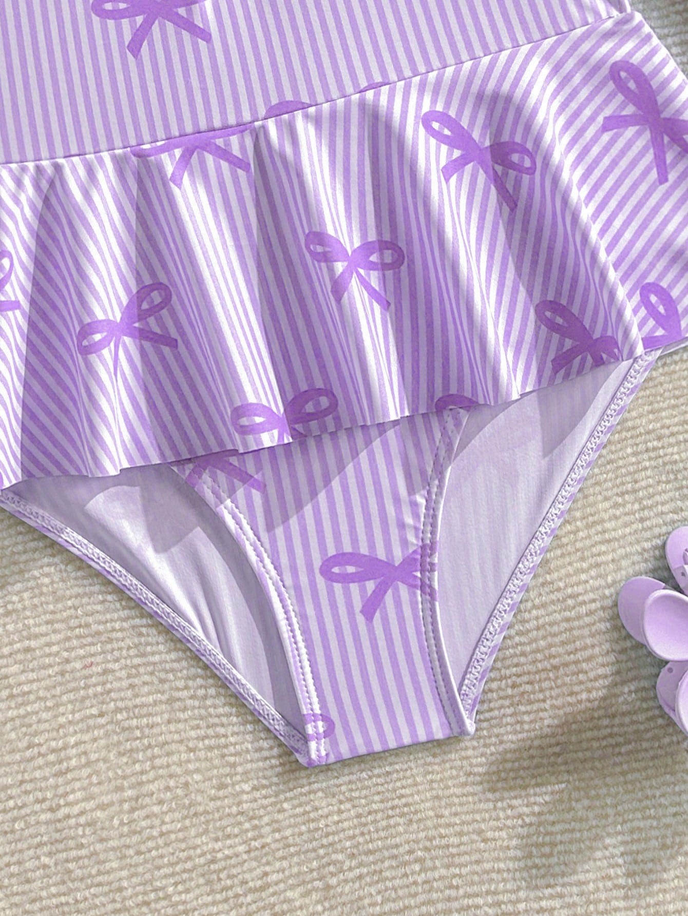 Purple tween girls one-piece swimsuit with graphic striped print, ruffle detail, round neck, and zipper closure for swimming and vacation wear
