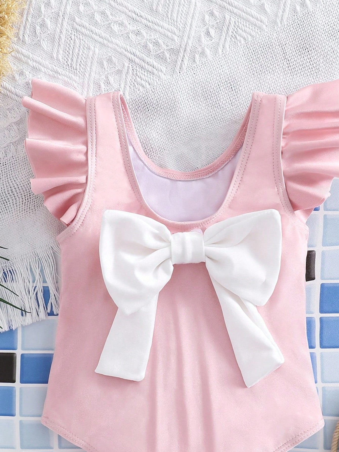 Baby pink colorblock one-piece swimsuit for tween girls with ruffle details, bow decor, scoop neckline, and fitted vacation swimwear style.