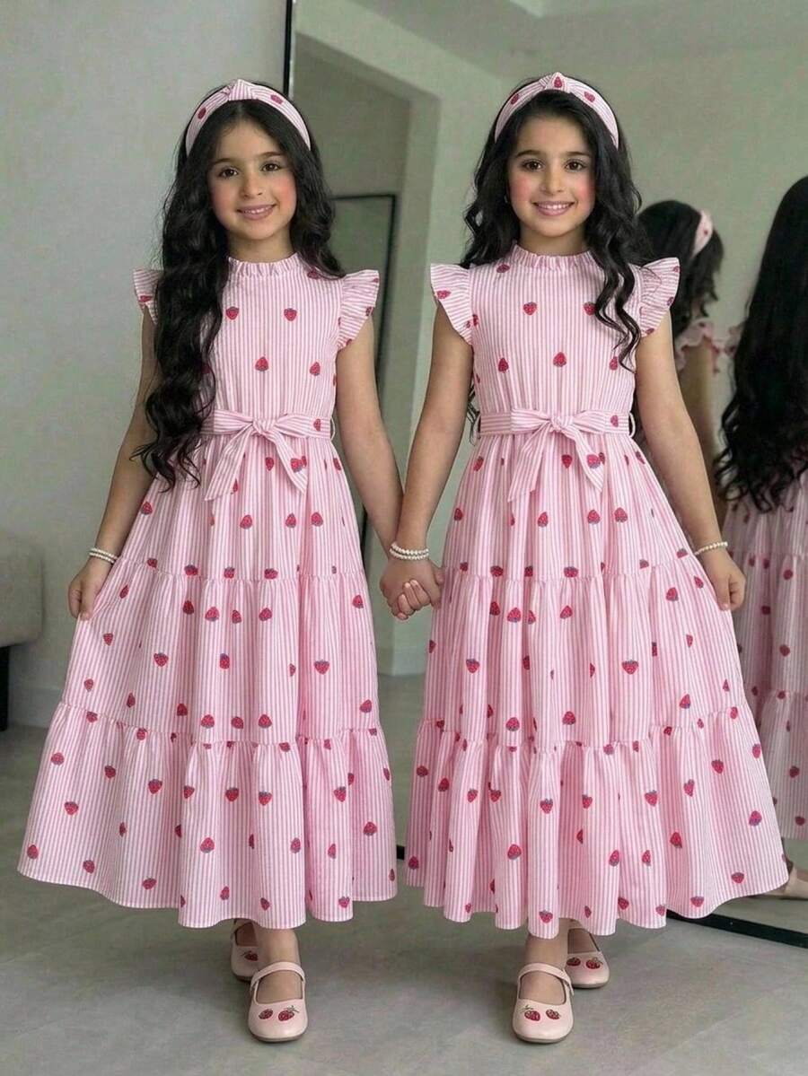 Tween girl wearing a pink long A-line dress featuring a strawberry print, stand collar, flounce short sleeves, and a belted waist with a ruffle hem.