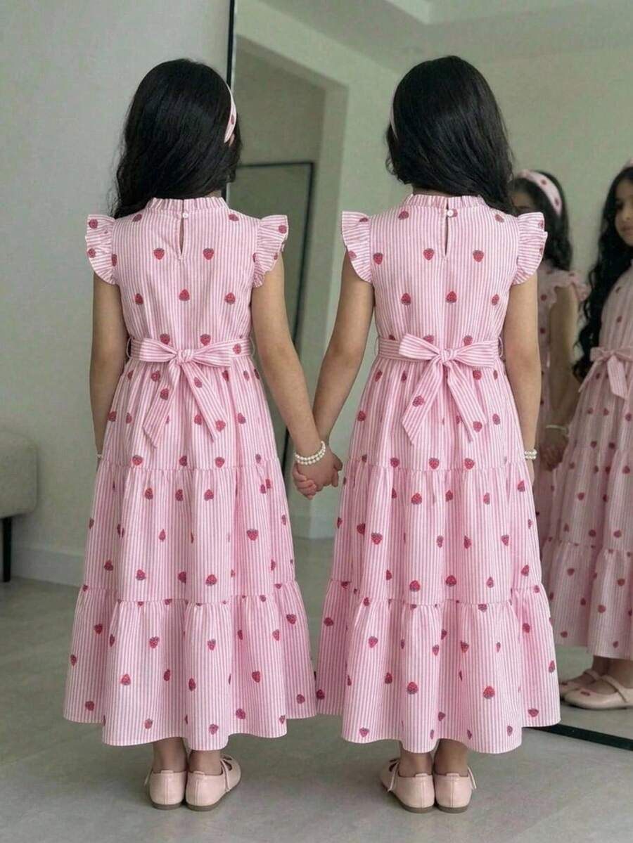 Tween girl wearing a pink long A-line dress featuring a strawberry print, stand collar, flounce short sleeves, and a belted waist with a ruffle hem.