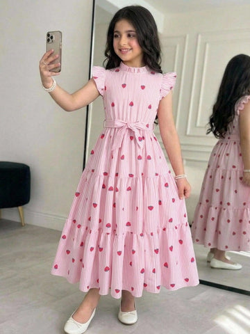 Tween girl wearing a pink long A-line dress featuring a strawberry print, stand collar, flounce short sleeves, and a belted waist with a ruffle hem.