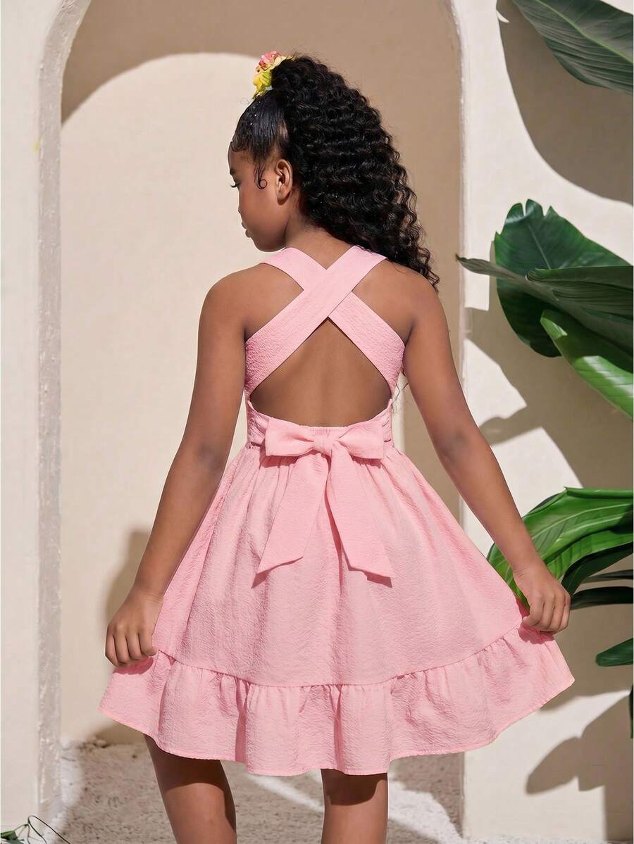 Pink sleeveless tween girls vacation dress with all-over fruit and vegetable print, strap neckline, belted high waist, cut-out detail, and flared ruffle hem.