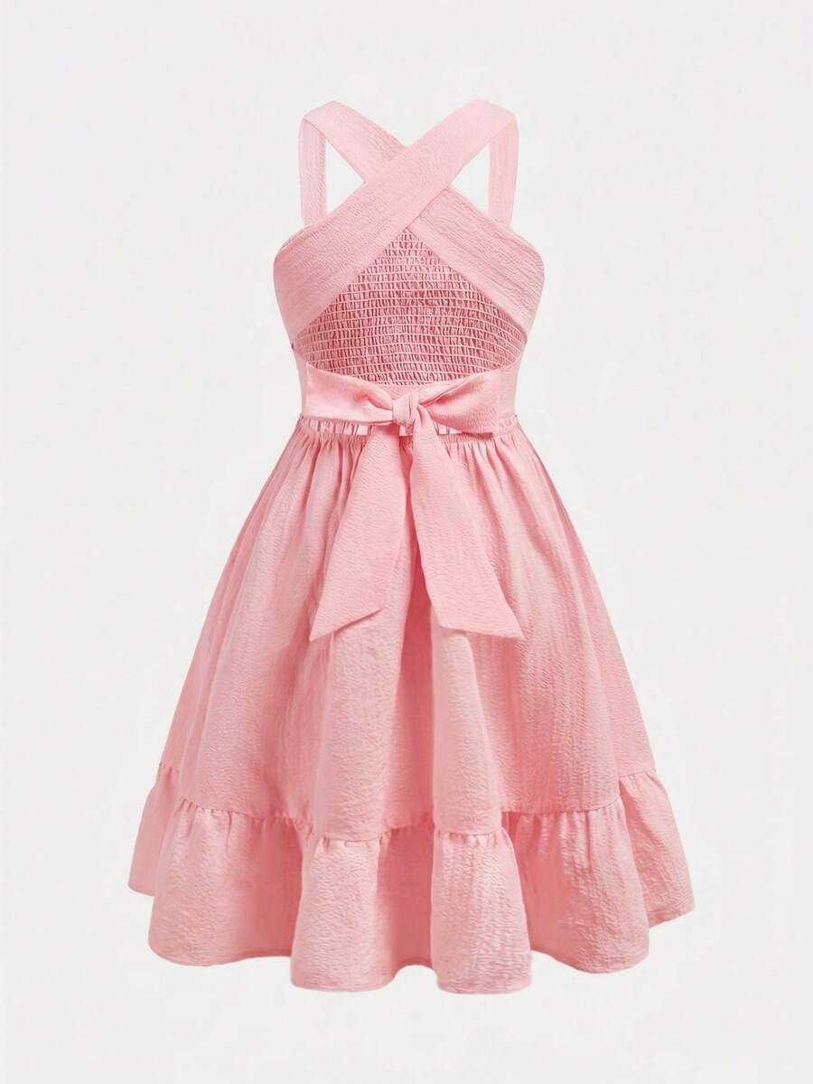Pink sleeveless tween girls vacation dress with all-over fruit and vegetable print, strap neckline, belted high waist, cut-out detail, and flared ruffle hem.