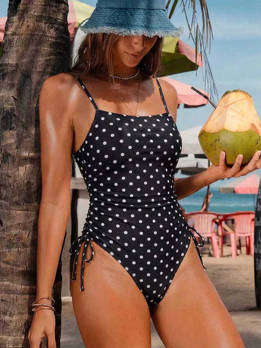 Women's retro 70s black and white polka dot one-piece swimsuit featuring a backless design, tie-front detail, spaghetti straps, and removable padding.