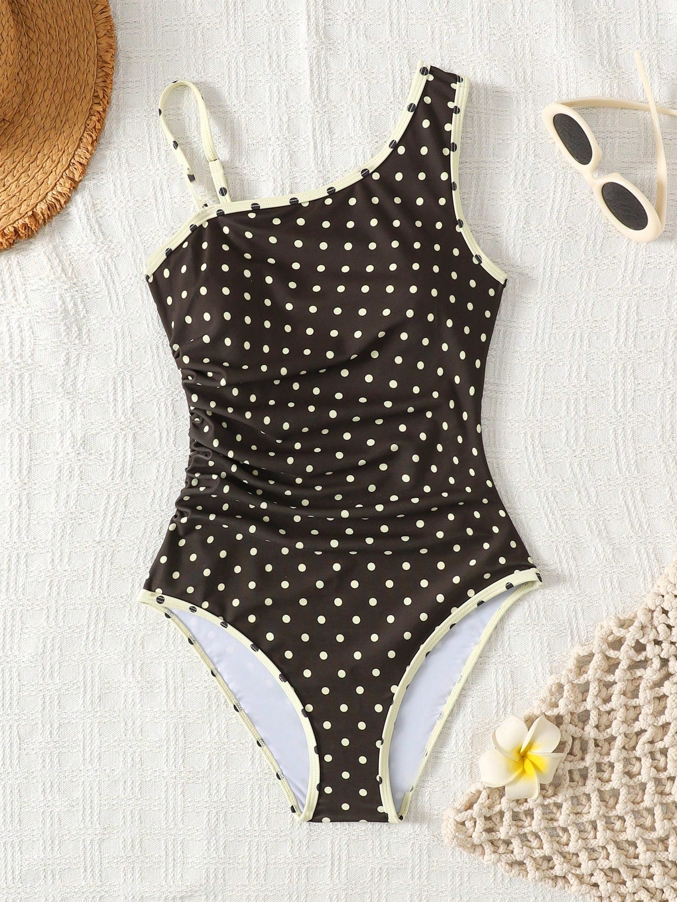 Tween girl one-piece swimsuit in brown polka dot geometric print with asymmetrical neckline, ruffle detail, cut-out design, and fitted mid-waist swim bottom.