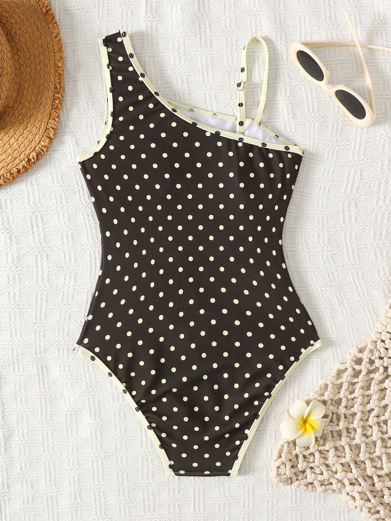 Tween girl one-piece swimsuit in brown polka dot geometric print with asymmetrical neckline, ruffle detail, cut-out design, and fitted mid-waist swim bottom.