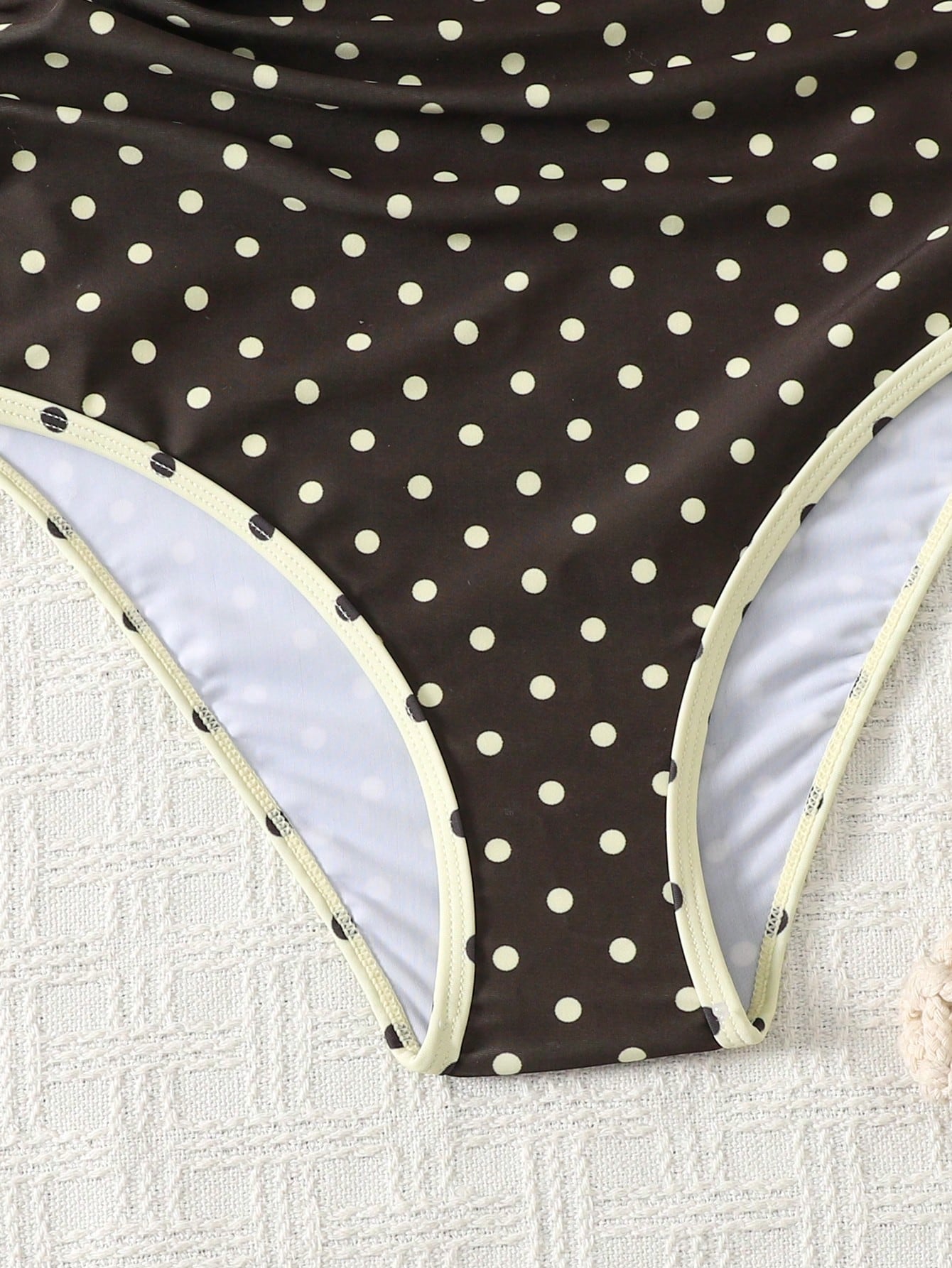Tween girl one-piece swimsuit in brown polka dot geometric print with asymmetrical neckline, ruffle detail, cut-out design, and fitted mid-waist swim bottom.