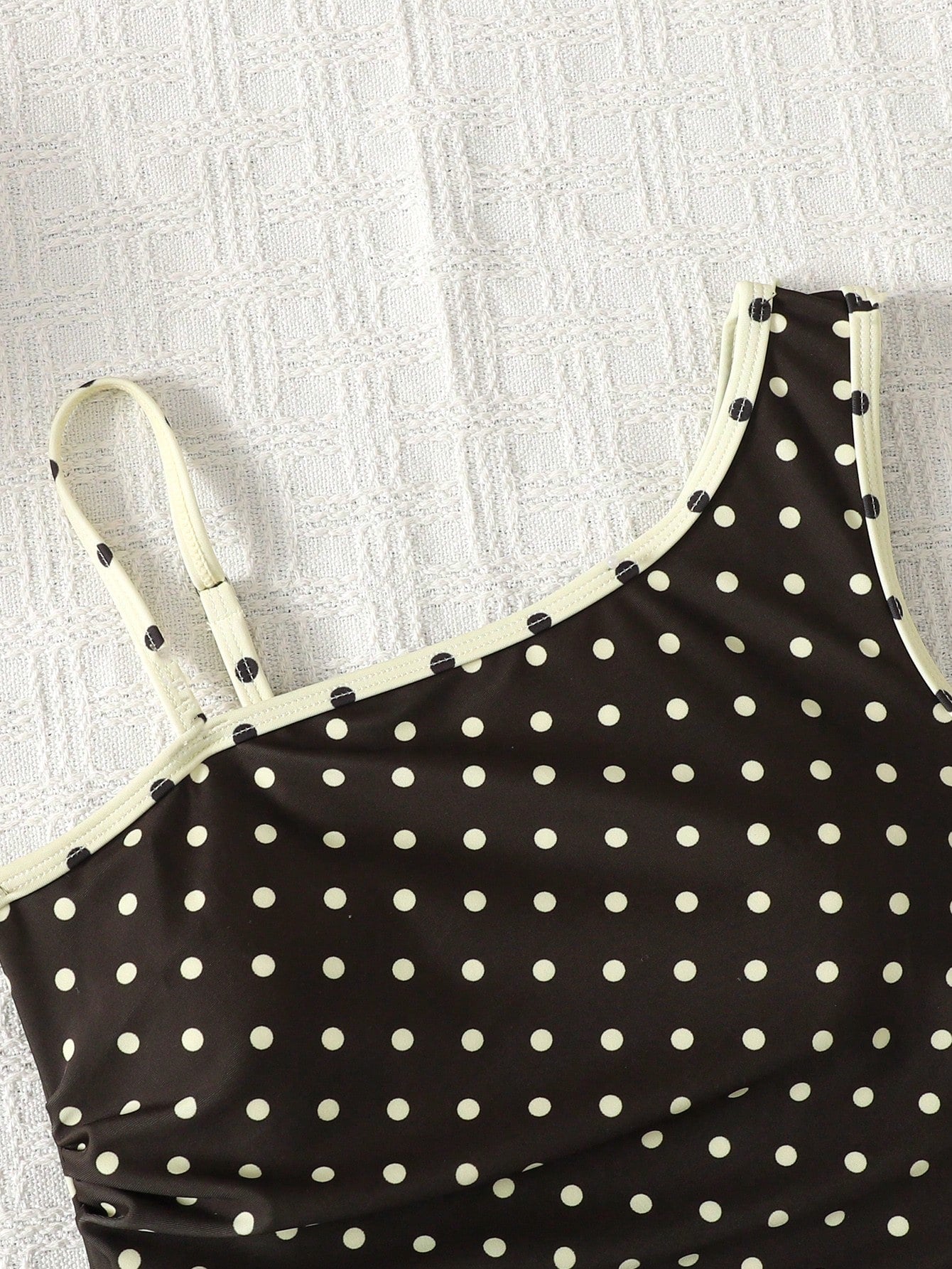 Tween girl one-piece swimsuit in brown polka dot geometric print with asymmetrical neckline, ruffle detail, cut-out design, and fitted mid-waist swim bottom.