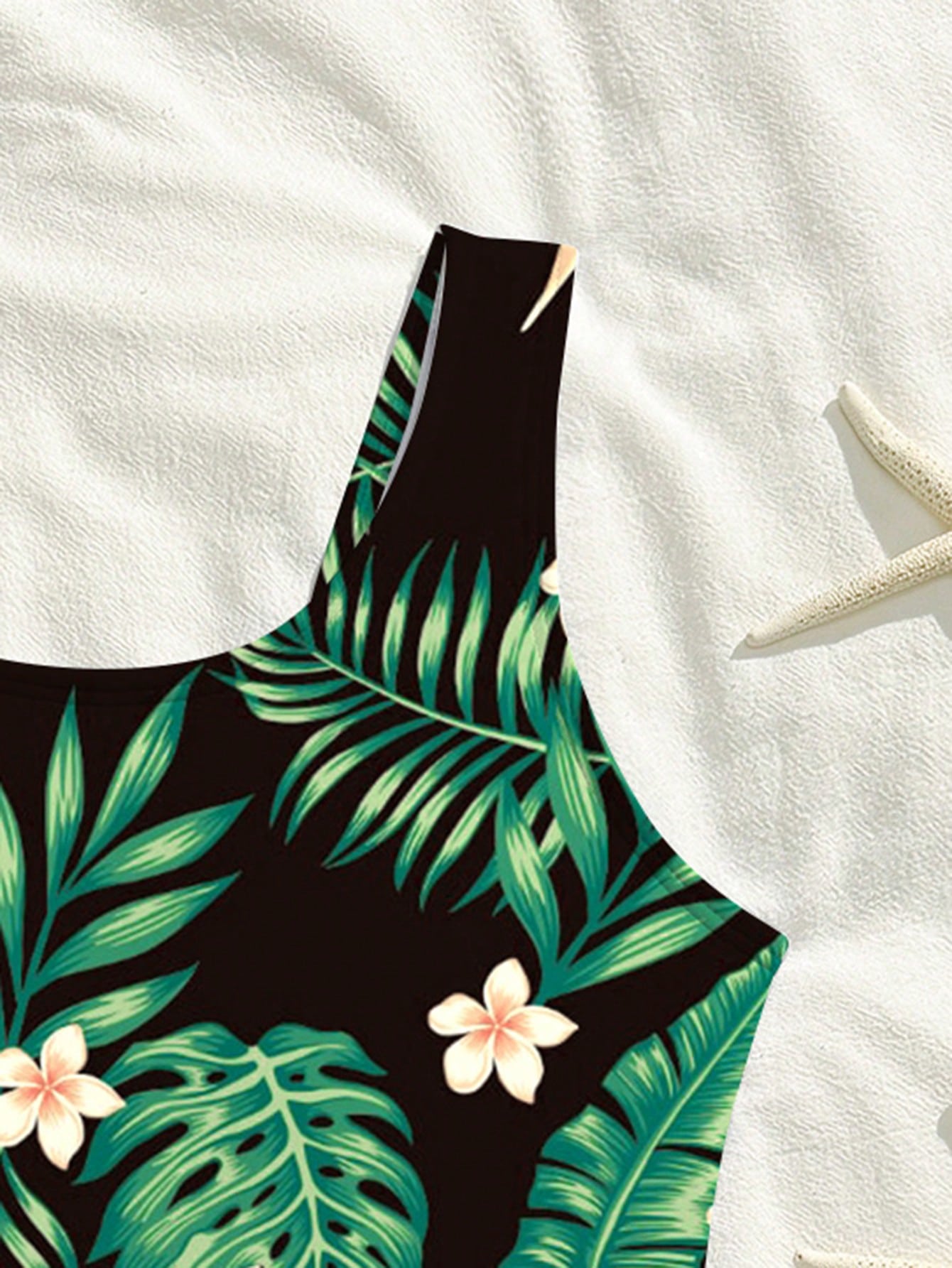Tween girls one-piece swimsuit with a black base and multicolor tropical plant print featuring bamboo, palm leaves, plumeria flowers, scoop neck, and wide straps.